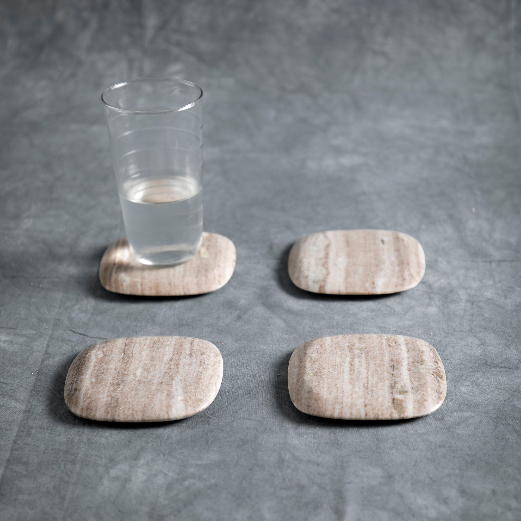 Four marble coasters with a water glass on top of one of them - trivets and coasters collection at Better World Bio