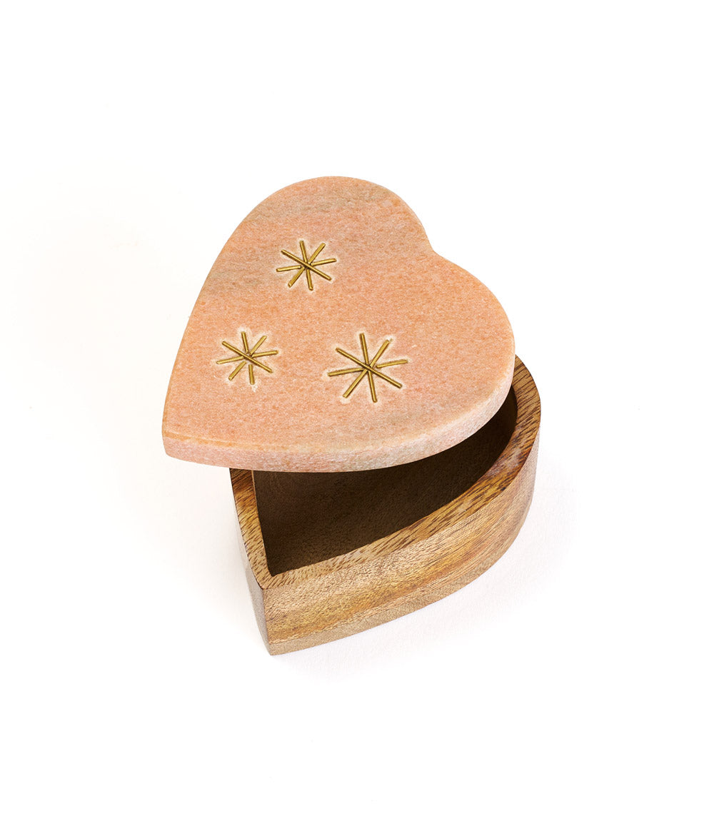 A heart-shaped pink marble keepsake box with brass stars inlay on the lid, set on a wooden base opened up.