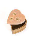 A heart-shaped pink marble keepsake box with brass stars inlay on the lid, set on a wooden base opened up.