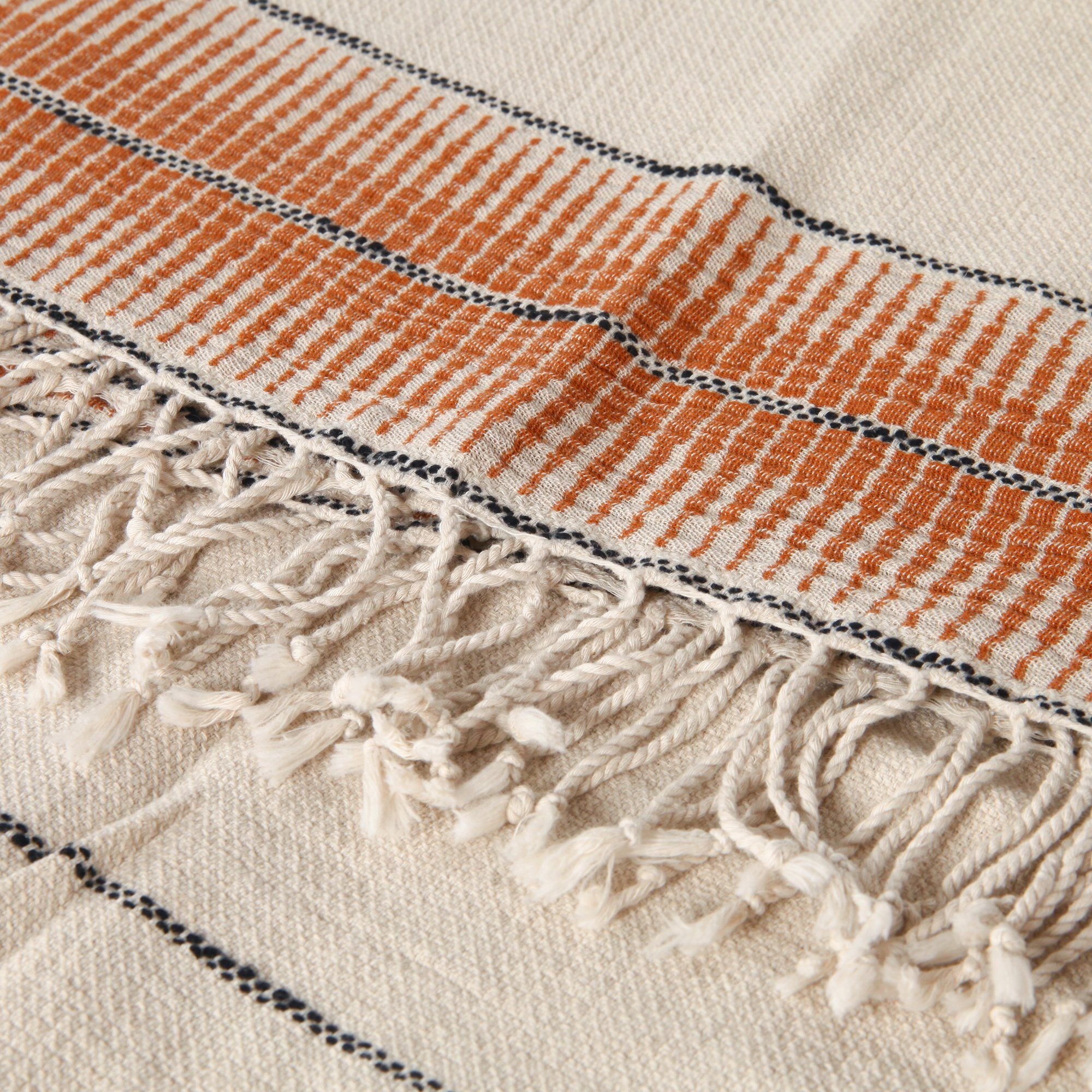 Textile with orange and black striped pattern and beige fringe on a white background