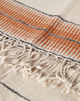 Textile with orange and black striped pattern and beige fringe on a white background