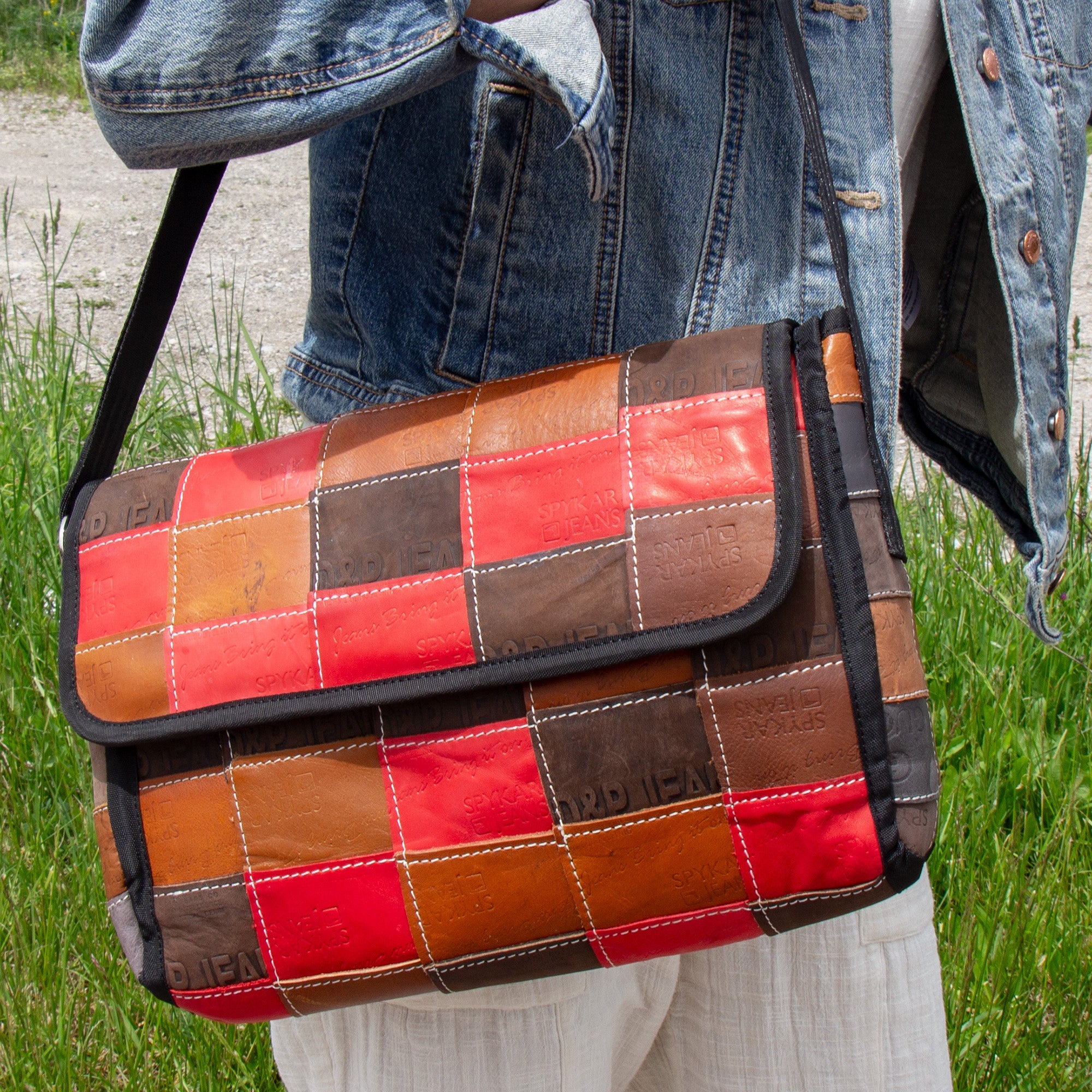 A person holding a crossbody bag with a patchwork design made from upcycled leather, featuring a black nylon strap and interior pockets, in brown, red, and blue colors.