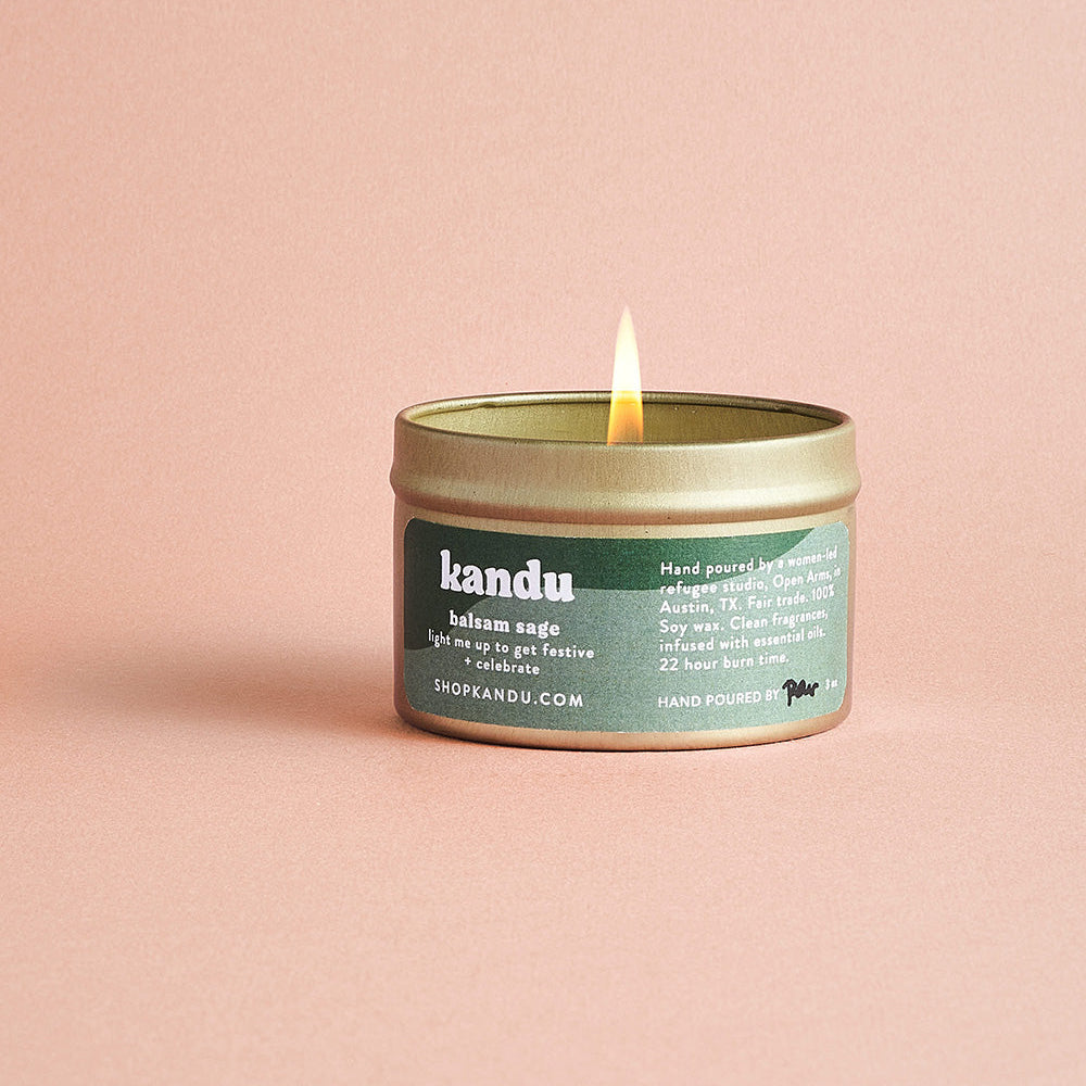 Kandu candle in a green container with a lit flame on a pink background