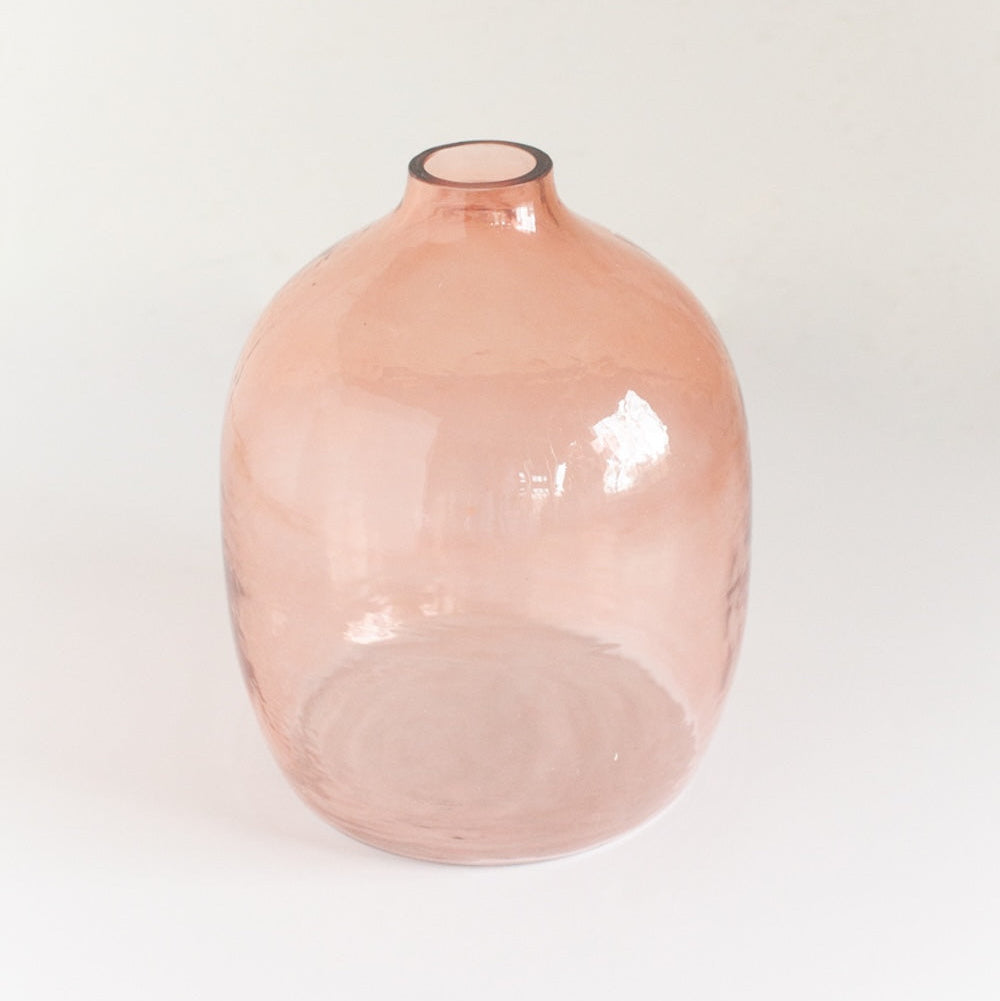 A blush-colored, hand-hammered glass vase with an oval shape on a white background.