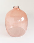 A blush-colored, hand-hammered glass vase with an oval shape on a white background.