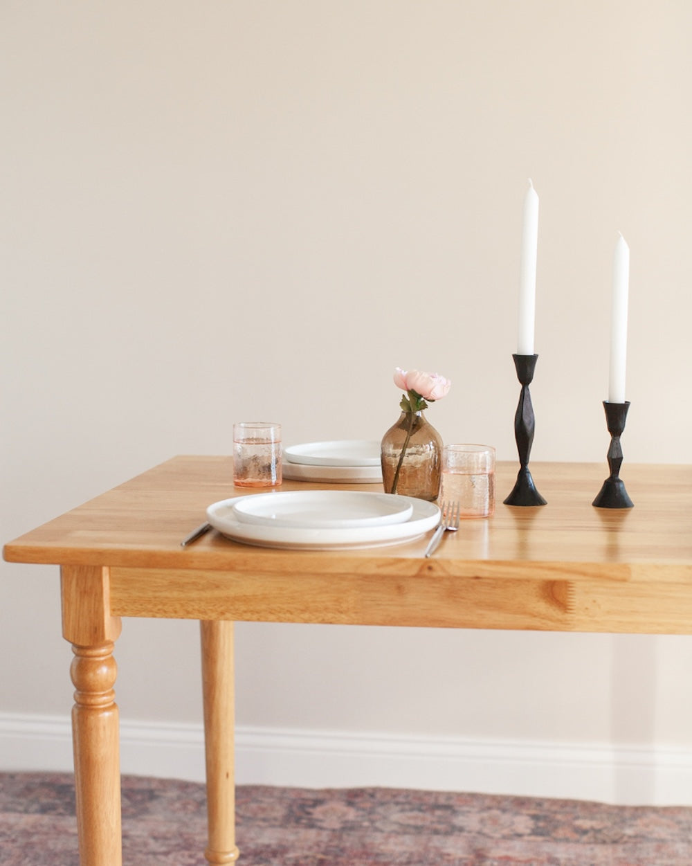 Dining table set with plates, glasses, and candles against a plain wall.