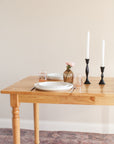 Dining table set with plates, glasses, and candles against a plain wall.