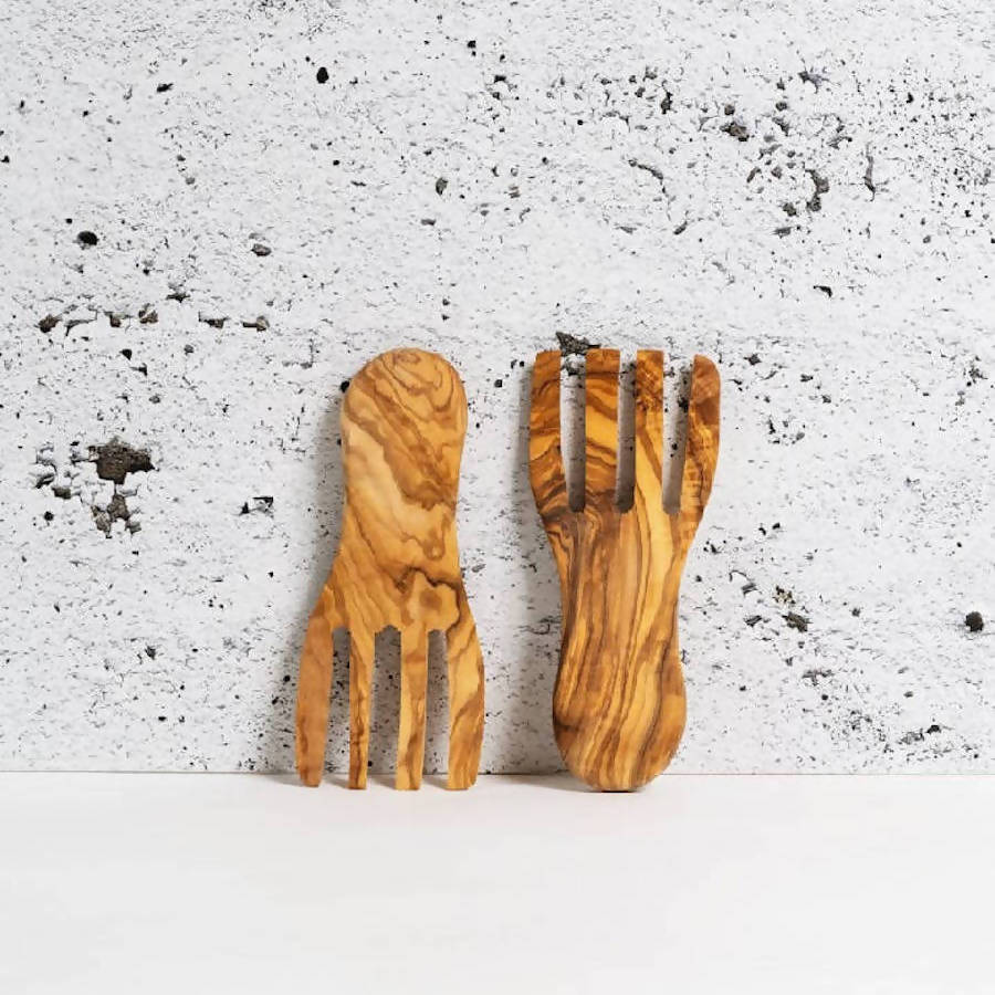 A pair of olive wood salad servers flat forks set against a concrete background