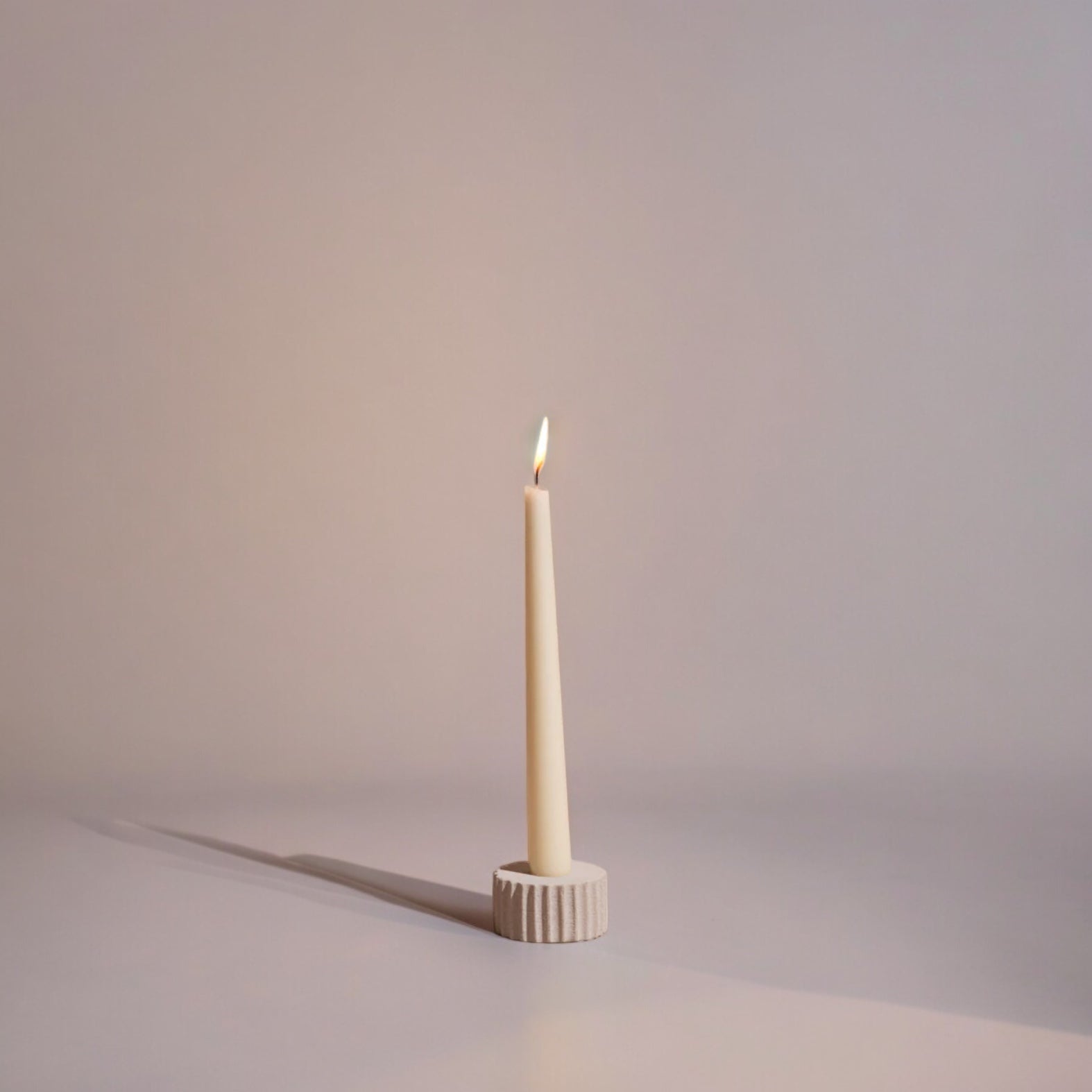 A natural sandstone taper candle holder with a white candle lit, set against a neutral background.