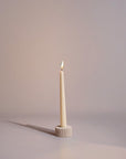 A natural sandstone taper candle holder with a white candle lit, set against a neutral background.