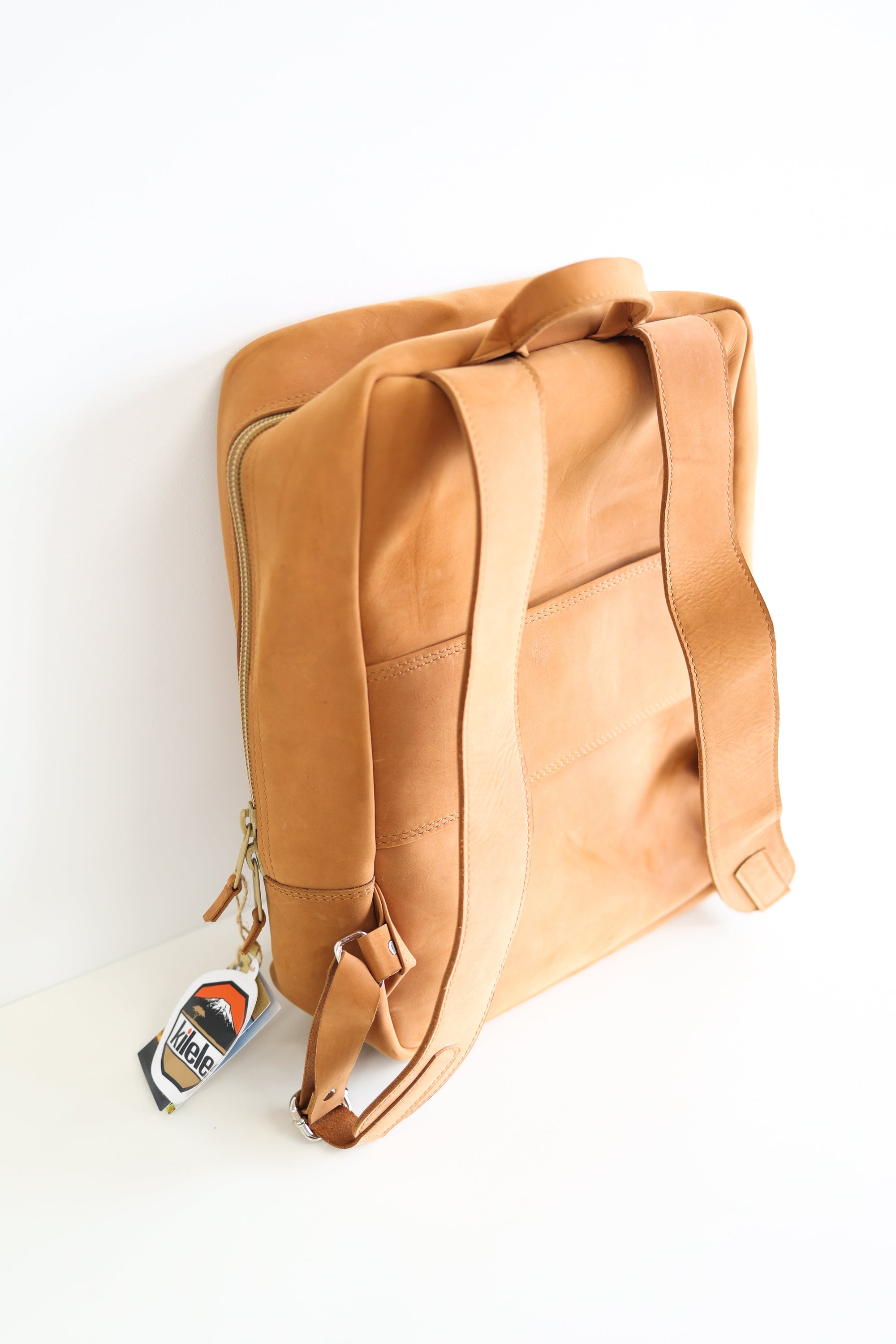 The back of a leather book bag in tan, displayed upright against a white background.