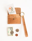 Brown leather wallet with keychain, money, and coins on a white background