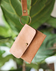 Brown leather wallet with strap against a blurred green leafy background