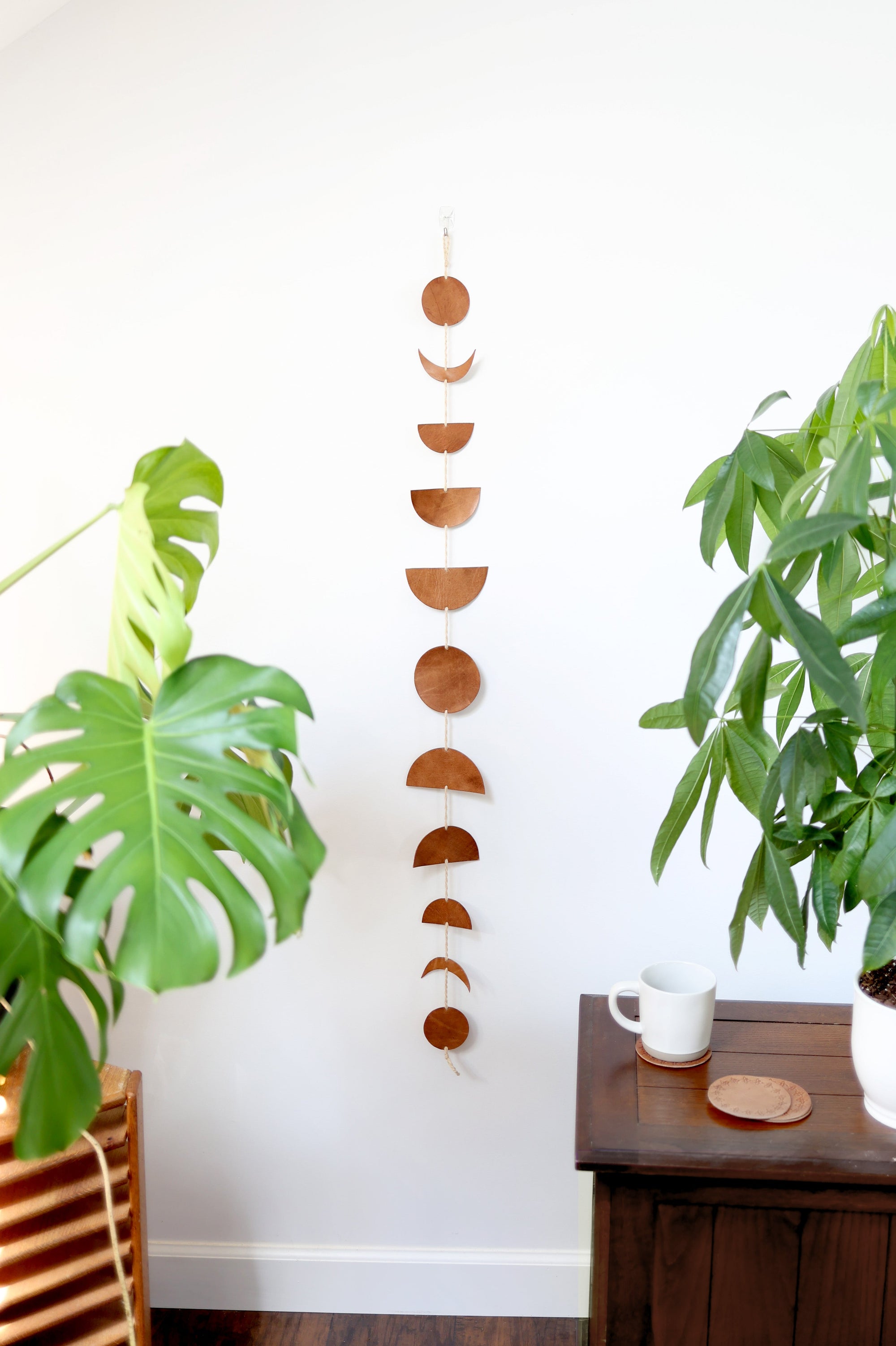 A garland featuring various phases of the moon made from brown leather hanging vertically on a wall