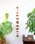 A garland featuring various phases of the moon made from brown leather hanging vertically on a wall