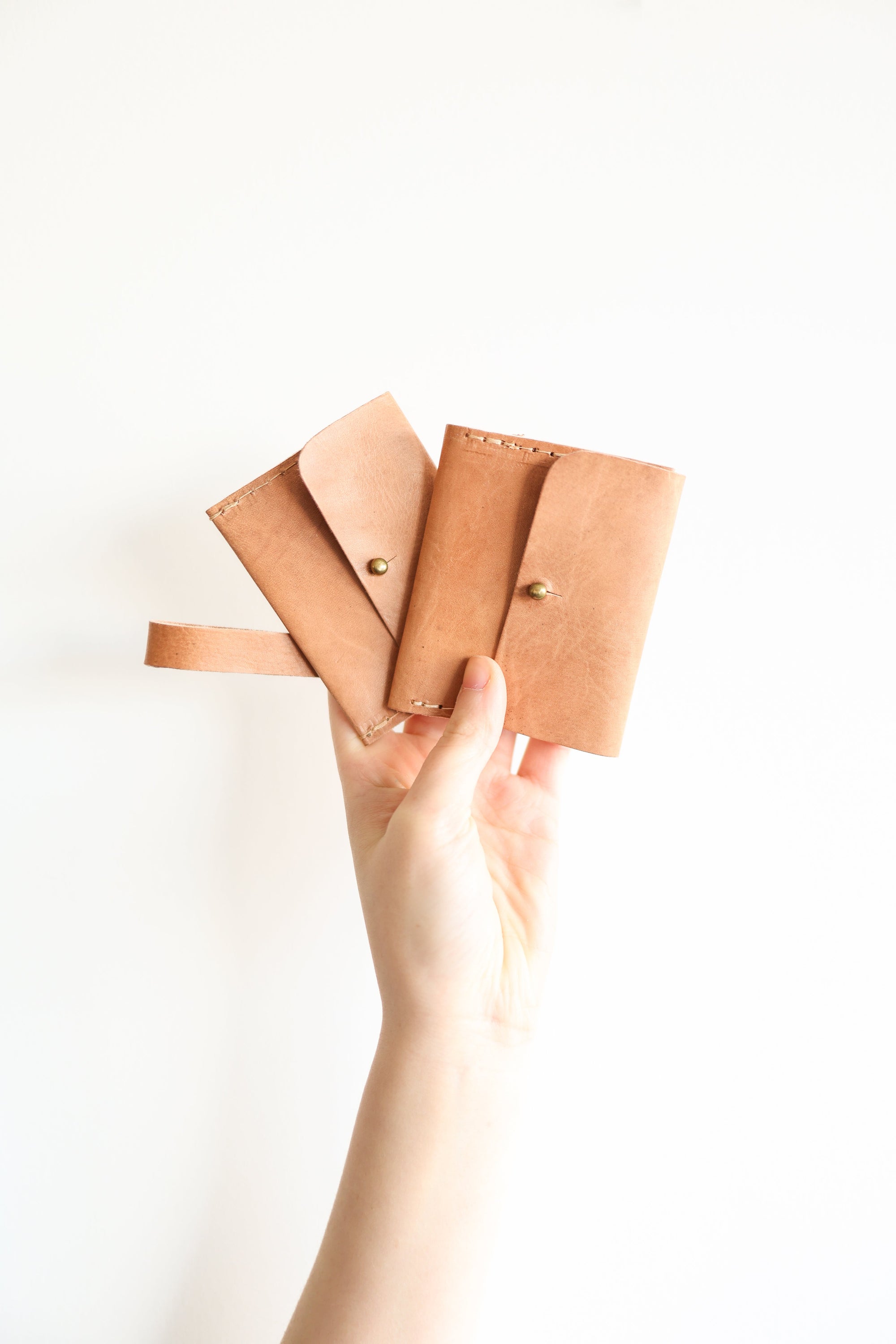 Hand holding three brown leather wallets against a white background