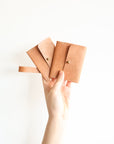 Hand holding three brown leather wallets against a white background