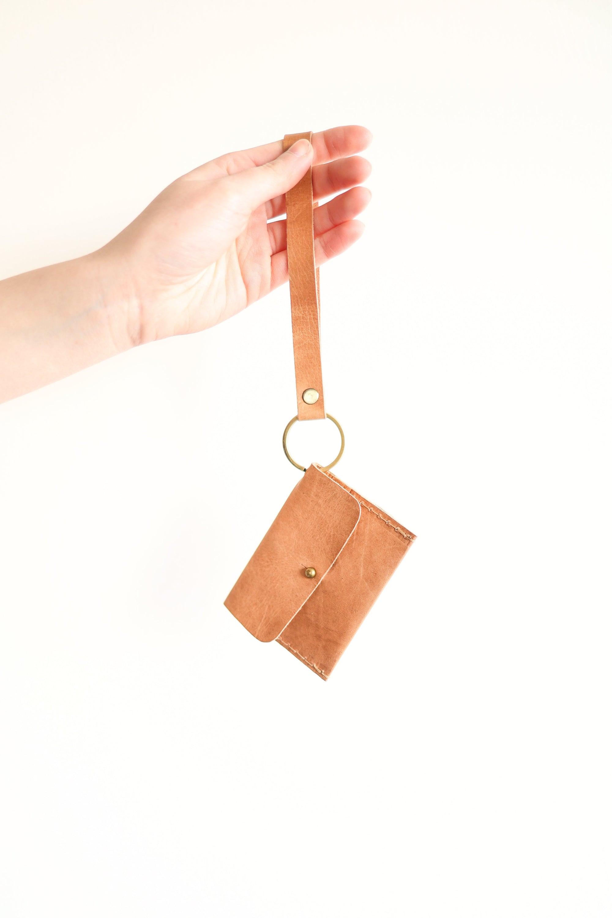 Brown leather wallet with strap held by a hand on a white background