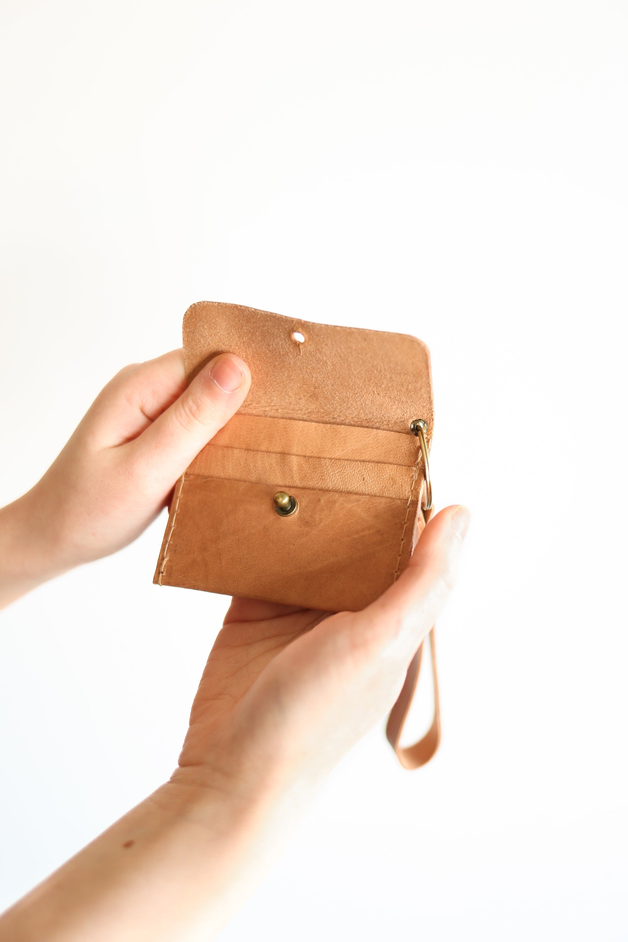 Brown leather wallet held by a hand on a white background