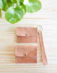 Pink leather wallet with strap on a light wooden surface with green leaves in the corner.
