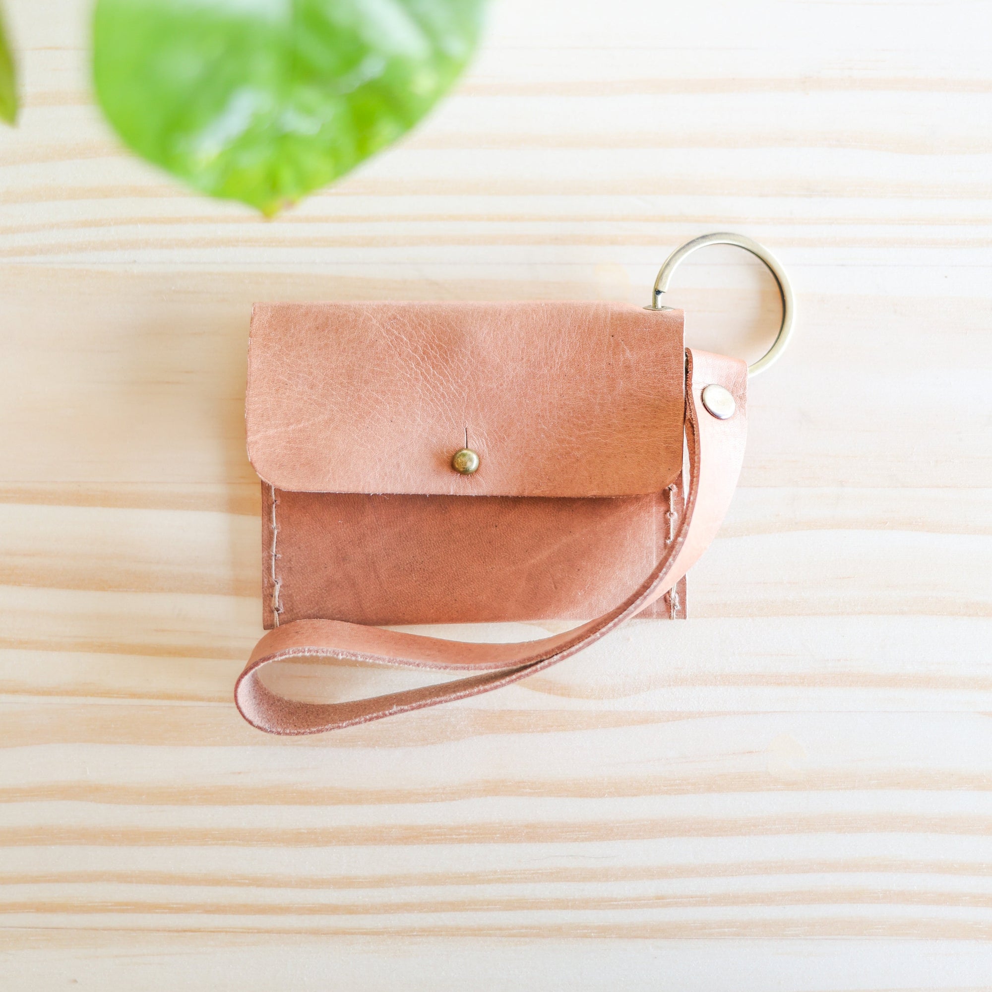 Small pink leather pouch with a strap on a light wooden surface with green leaves in the corner.
