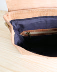 Close-up of a beige leather bag with a navy interior on a light wooden surface.