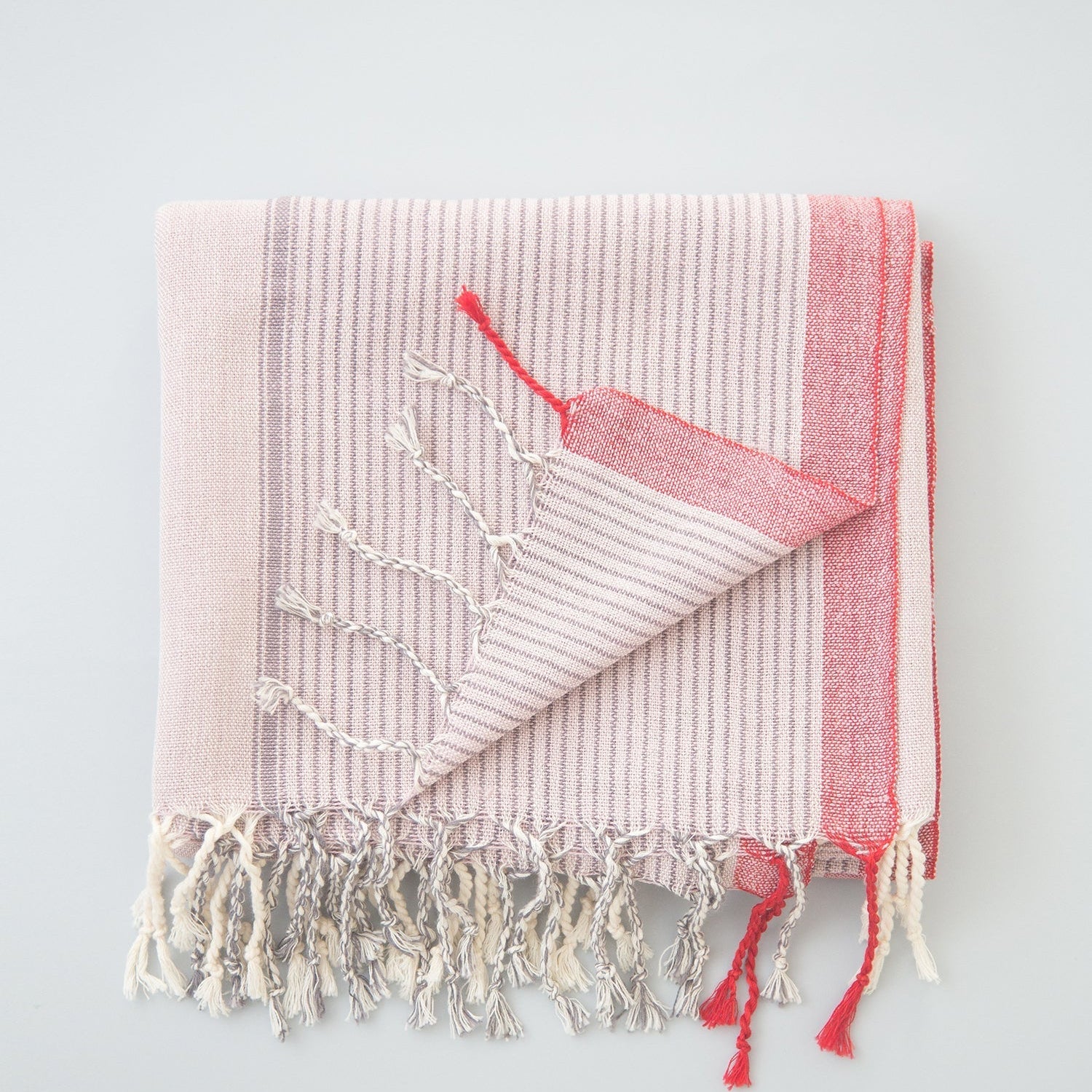 A handwoven Turkish towel in pink and white with a geometric pattern and fringes on the edges