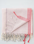 A handwoven Turkish towel in pink and white with a geometric pattern and fringes on the edges