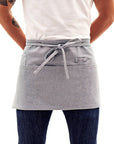 A person wearing a blue waist apron with multiple pockets and a utility loop, standing against a white background.