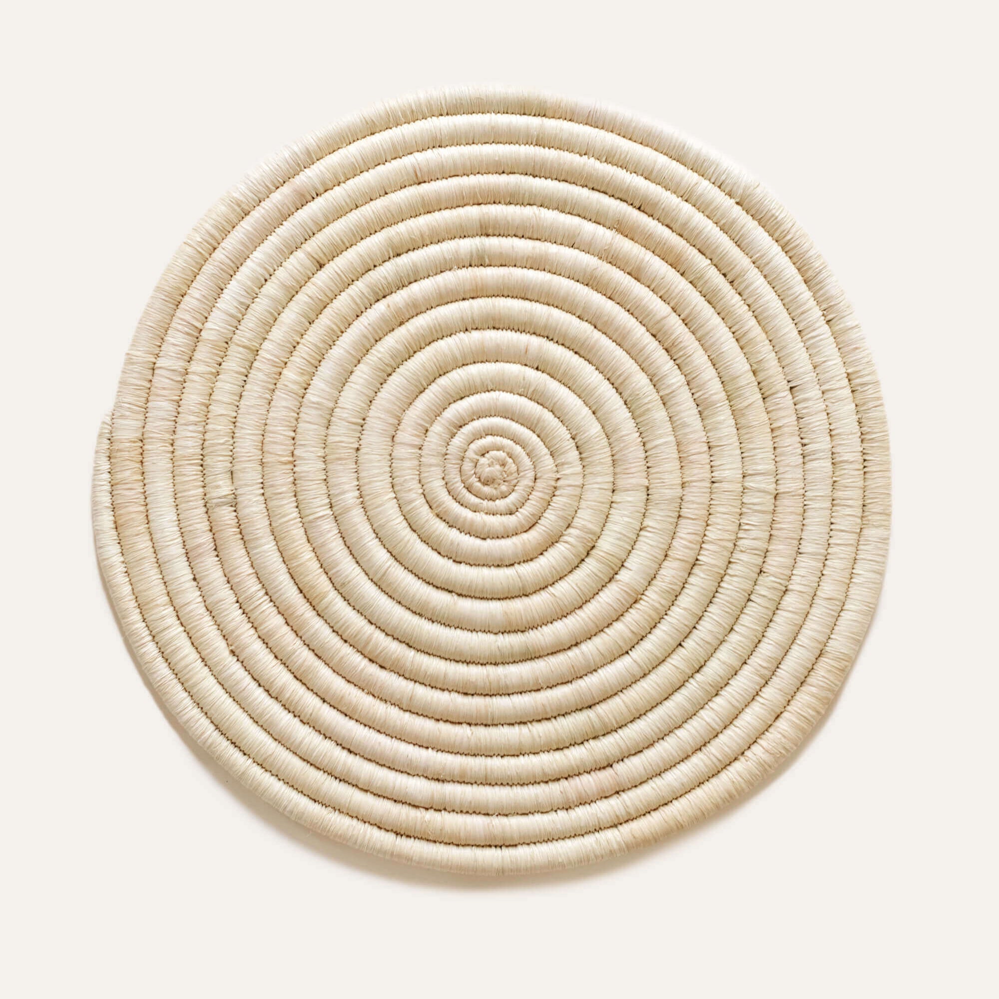 A circular natural raffia placemat with a spiral pattern, displayed on a white background