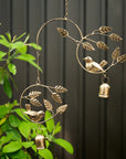 Decorative metal wind chime with birds and leaves against a dark background
