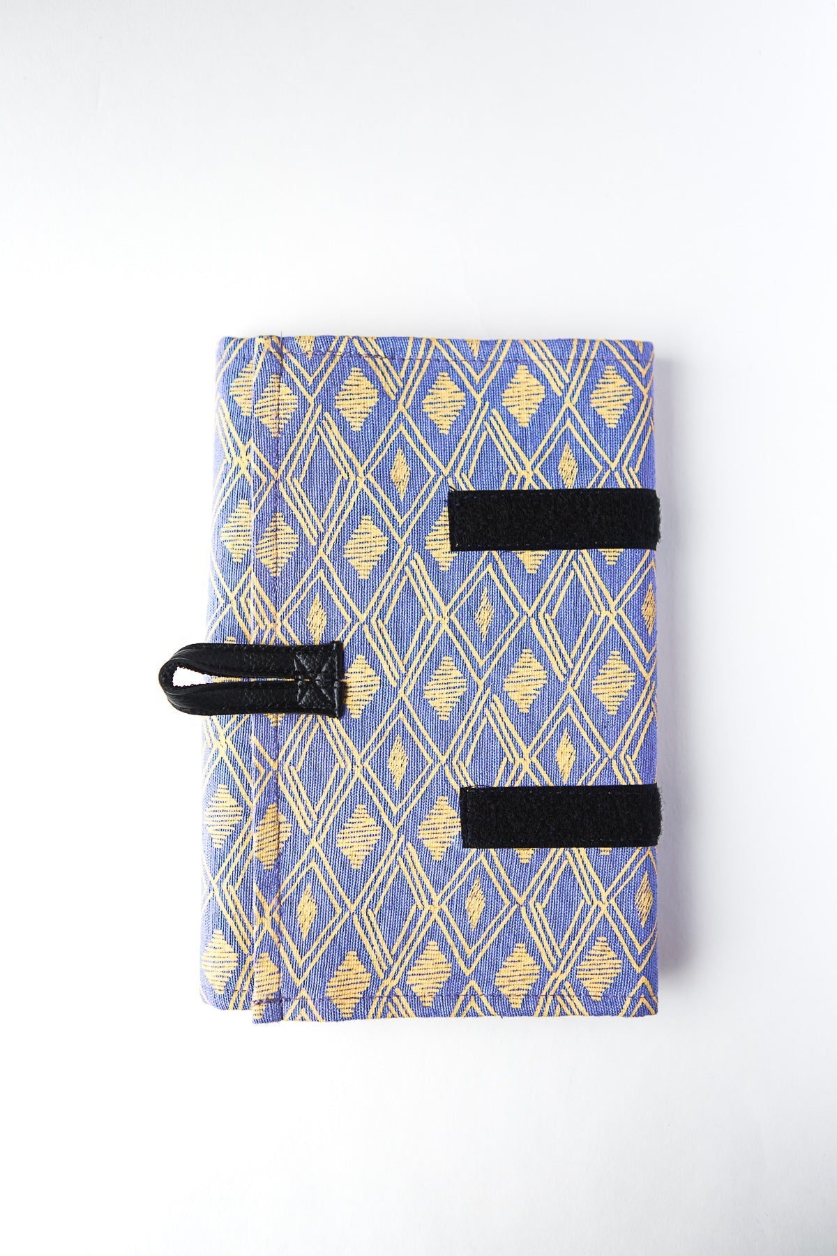 A closed jewelry roll travel case with various compartments for earrings, rings, and necklaces, displayed alongside some jewelry items and a patterned fabric.