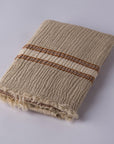 A hand loomed muslin linen beach towel with blue and green stripes, hanging on a rod against a white wall.