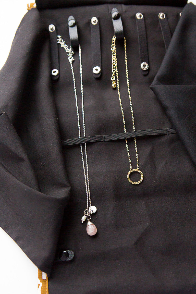 Necklaces shown in a jewelry roll travel case with chevron pattern, unrolled to show compartments for earrings, rings, and necklaces, with jewelry items like earrings, rings, and necklaces organized within it.