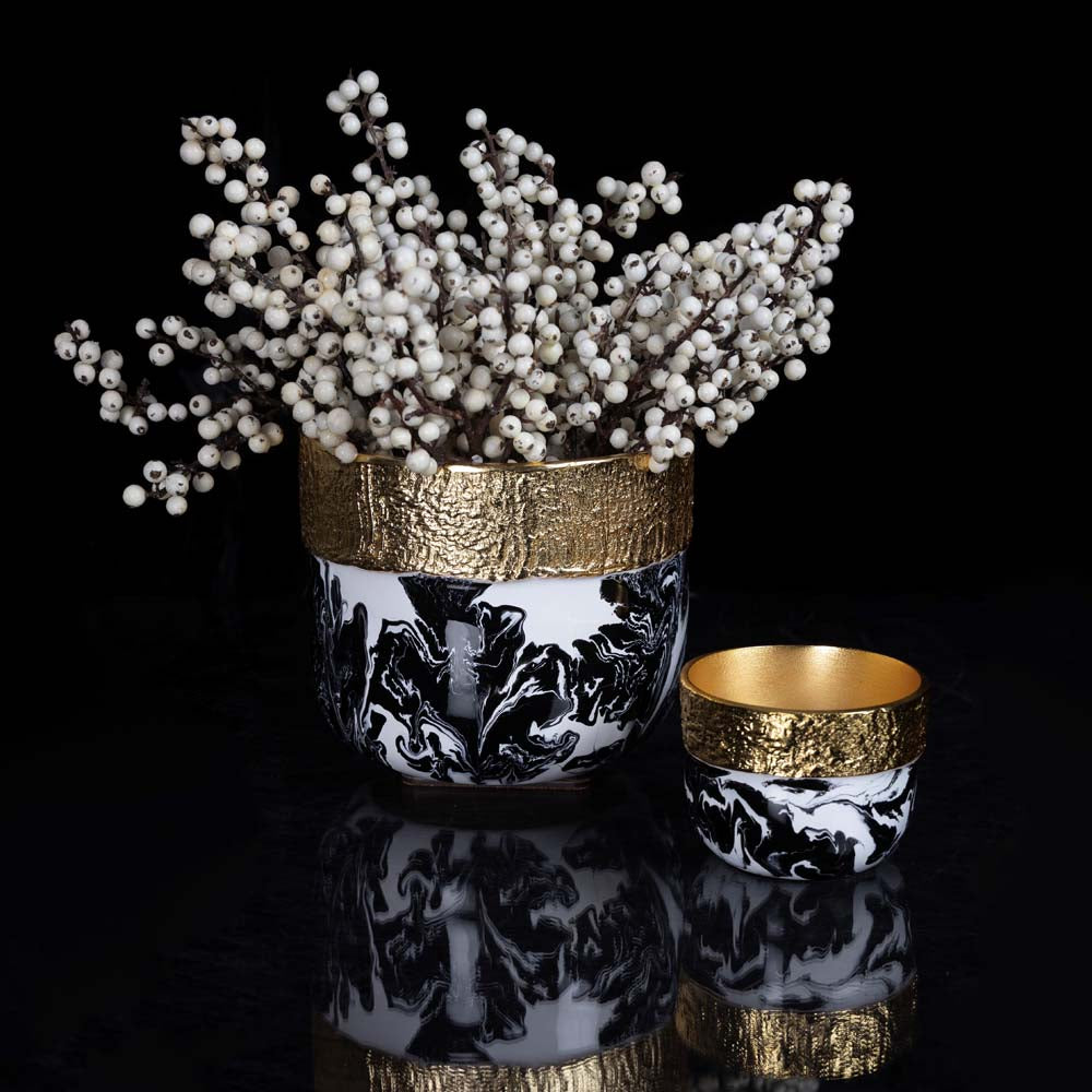 Decorative vase with gold rim and black and white design, accompanied by a small bowl with gold rim on a reflective surface.