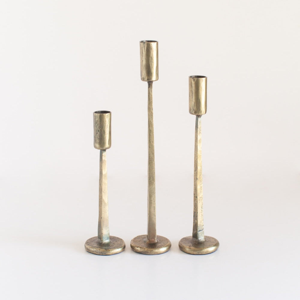 A set of three brass finish iron candle holders in varying heights, with a textured surface and a round base.