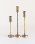 A set of three brass finish iron candle holders in varying heights, with a textured surface and a round base.