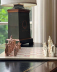 A hand-carved soapstone chess set with a green and pink checkered board and beige, pink, and white stone pieces zoomed in on the white pieces on a table near a lamp.