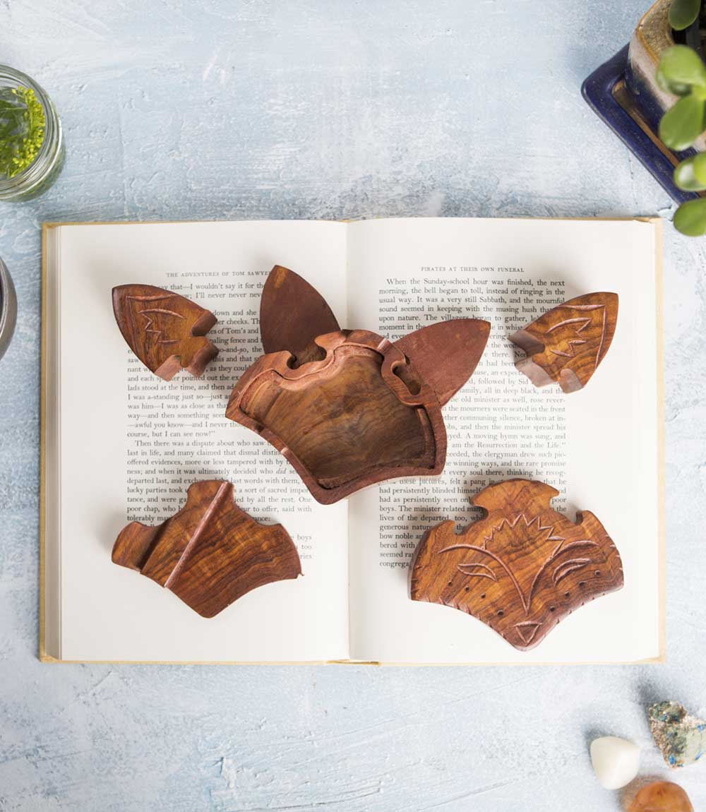 The puzzle pieces of a hand-carved wooden fox face puzzle box on top of a book.