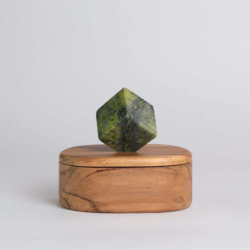 Wooden box with a green geometric stone on top against a light gray background