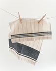 A striped cotton tea towel hanging on a clothesline with two wooden clothespins