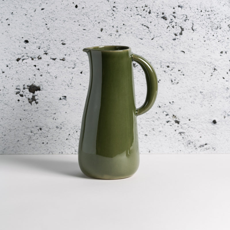 A green stoneware jug with a handle and spout on a textured black and gray background