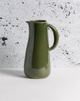 A green stoneware jug with a handle and spout on a textured black and gray background