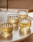 A set of four clear mouth-blown glass cups with a bud-like shape and wave-like rim, displayed on a tray
