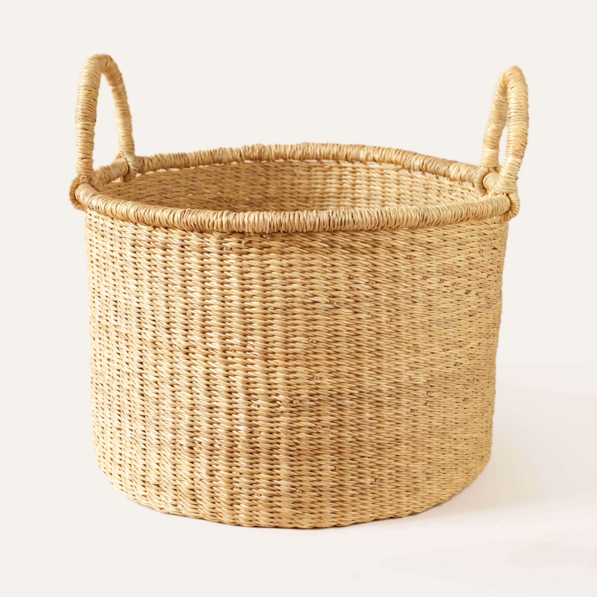 A beige Bolga floor basket with handles made from natural color grasses