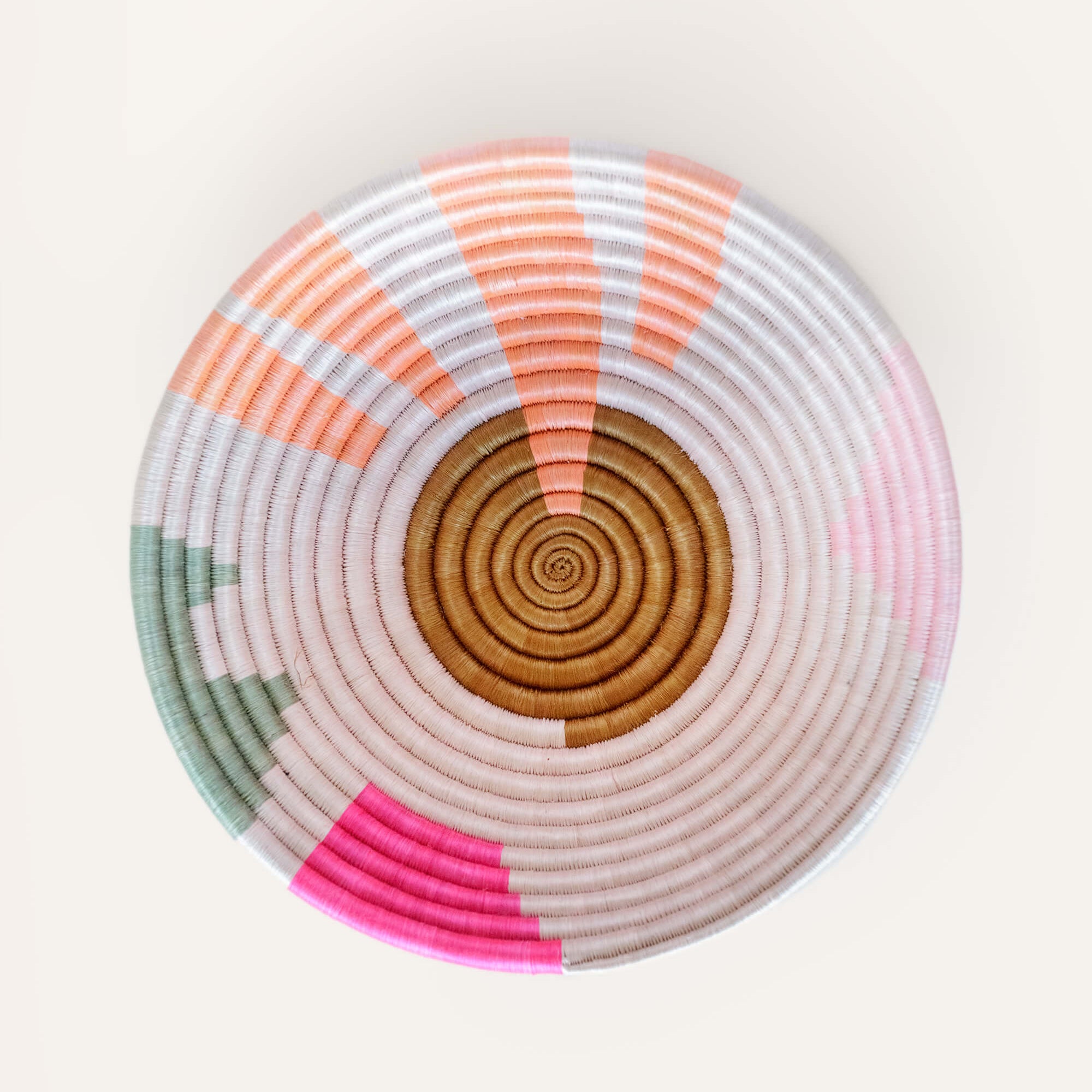 A handwoven geometric basket with light blush, pink, coral, and green accents, made from strands of sisal wrapped around bunches of sweetgrass