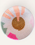 A handwoven geometric basket with light blush, pink, coral, and green accents, made from strands of sisal wrapped around bunches of sweetgrass