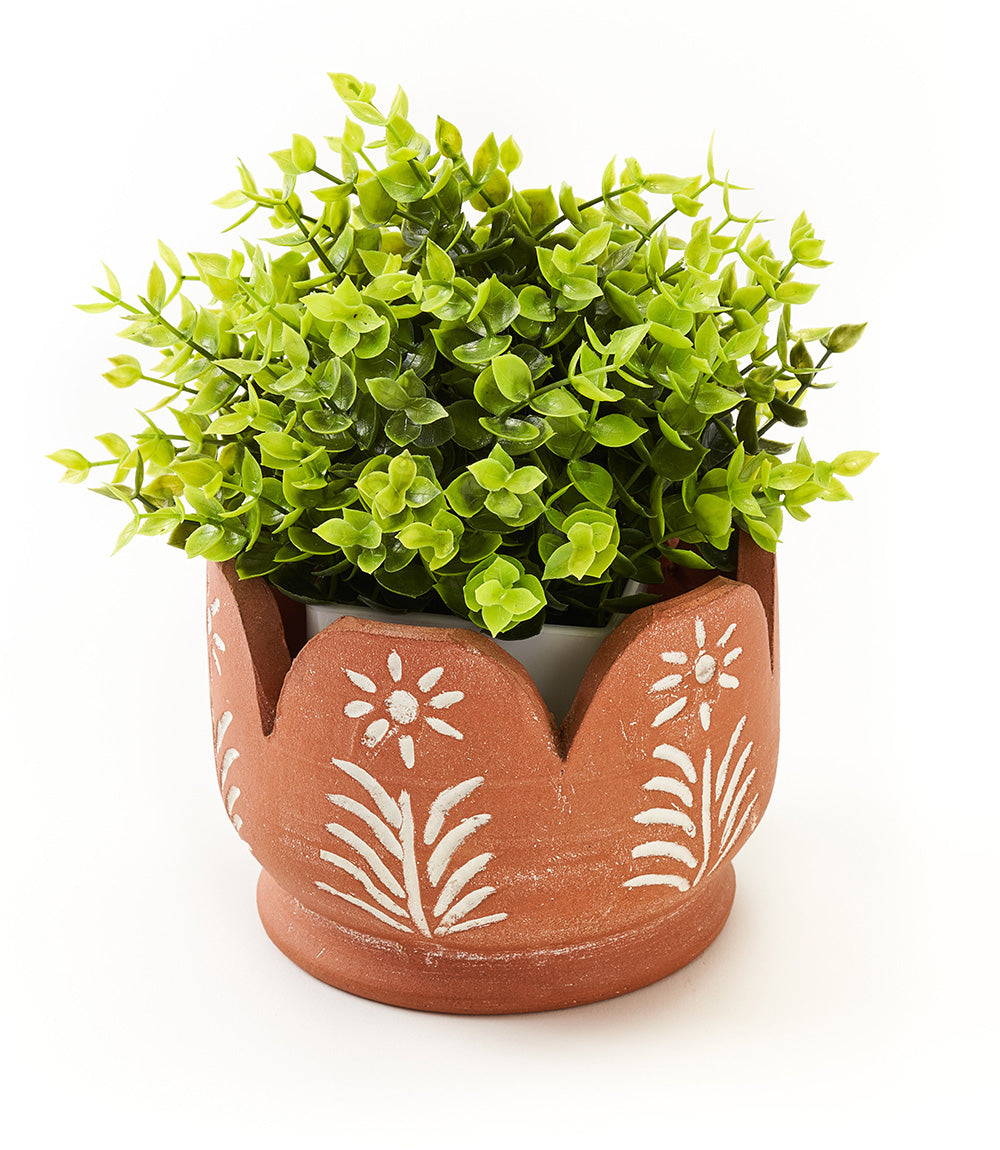 A terracotta planter with hand painted petal accents, containing green plants.