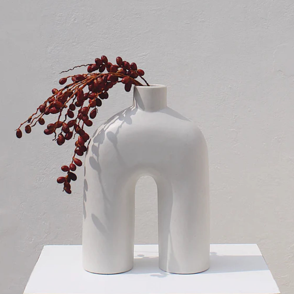 A white, handmade ceramic vase holding red flowers
