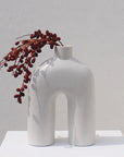 A white, handmade ceramic vase holding red flowers